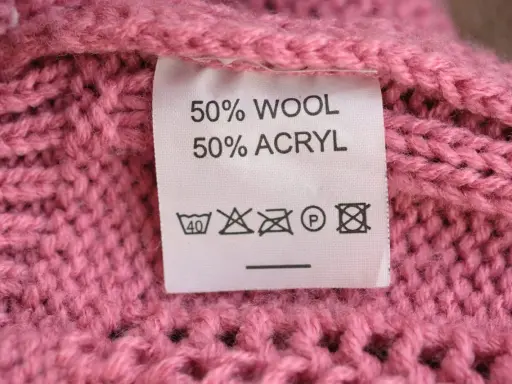 En rosa stickad tröja med en etikett som visar 50% ull och 50% akryl.