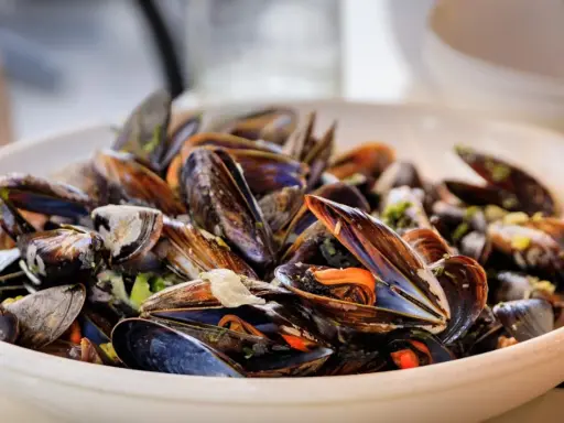 Un plato rebosante de mejillones al vapor, con sus conchas abiertas mostrando la carne anaranjada y jugosa.