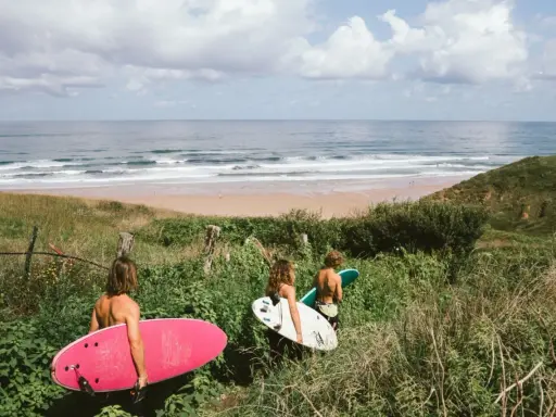 Drei Freunde mit Surfbrettern auf dem Weg zum Strand in Spanien. Die Wellen laden zum Surfen ein.