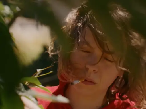 En närbild på Nina Widerberg med en cigarett i munnen, omgiven av gröna blad.