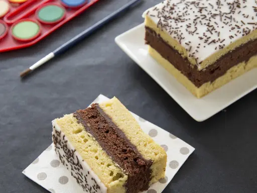 Gâteau napolitain, le meilleur pâtissier. Une part sur une serviette, une autre entière sur une assiette. Pinceau et palette de peinture à proximité.