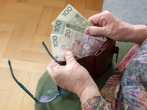 Dłonie starszej osoby wyciągają pieniądze z portfela. Widać banknoty 100 zł i 20 zł, być może to oczekiwana trzynasta emerytura.