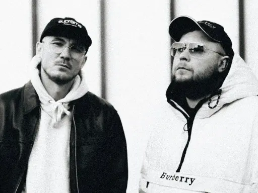 Dwóch mężczyzn w czapkach i okularach. Jeden w skórzanej kurtce, drugi w białej bluzie z kapturem. Pezet został ojcem, a jego przyjaciel świętuje z nim ten radosny moment.
