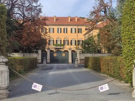 Ingresso di Villa San Martino ad Arcore, con cancello verde e alberi autunnali. Catena con cartelli di divieto di sosta blocca l'accesso.