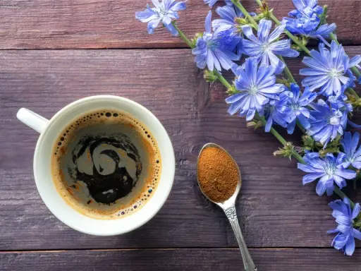 Taza de café de achicoria, con flores azules y una cucharada de polvo de achicoria, ideal para aprender como preparar achicoria en cafetera.