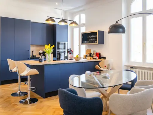 Élégante petite cuisine ouverte avec îlot central bleu marine, tabourets en bois et table en verre.