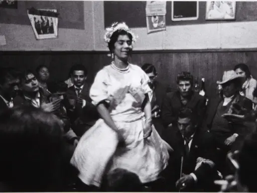 Una mujer con corona de flores baila en una celebración, rodeada de gente. Podría ser una boda gitana.