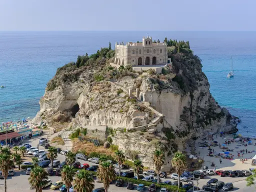 Santuario di Santa Maria dell'Isola a Tropea, regione Calabria, su uno sperone roccioso a picco sul mare azzurro, con spiaggia e palme.
