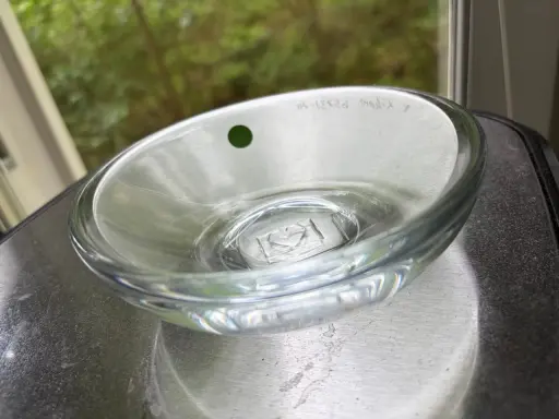 En Orrefors skål, ett tidlöst konstverk. Denna glasdesign med en grön prick och graverad text visar Orrefors skålar genom tiderna.