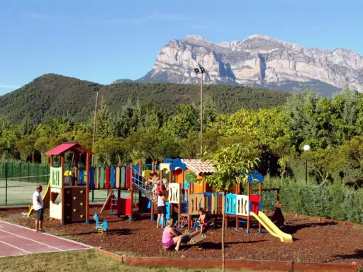 Parque infantil colorido en un camping de Huesca, con niños jugando y montañas imponentes al fondo.