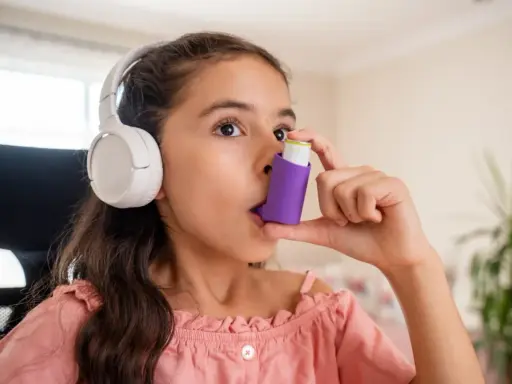 Mädchen mit Kopfhörern benutzt Inhalator gegen Asthma durch Stress.