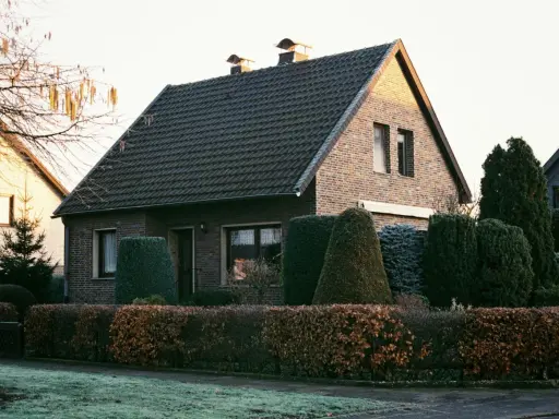 Ein gepflegtes Einfamilienhaus mit Ziegelfassade und dunklem Dach. Die Frage "wie viel kostet ein haus" wird durch die idyllische Szenerie aufgeworfen.