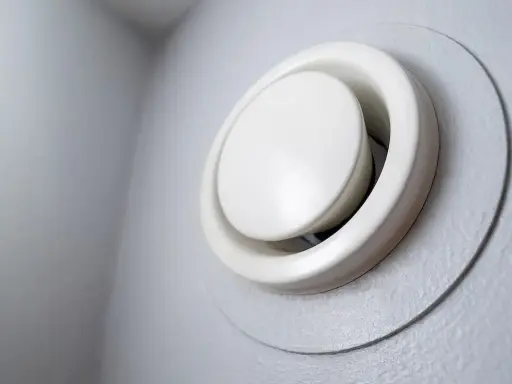 Grille de ventilation blanche, ronde et réglable, fixée sur un mur gris. Un système vmr hygroréglable pour une meilleure qualité de l'air.