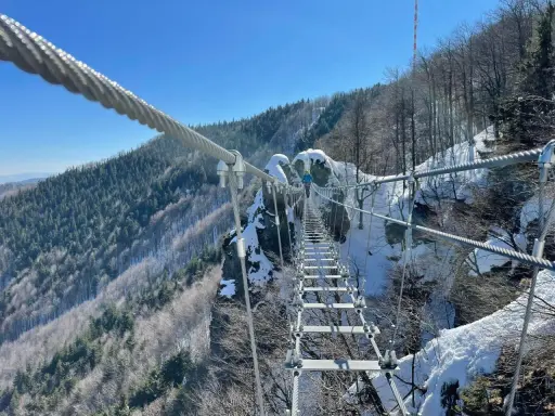 Zimowa przygoda na wiszącym moście nad przepaścią. Skalka pri Kremnici w śnieżnej odsłonie, z widokiem na zalesione zbocza.