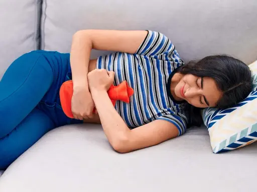 Joven con bolsa de agua caliente en el abdomen, aliviando el dolor de cólicos.