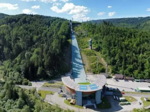 Skocznia narciarska w otoczeniu zielonych lasów, która latem pokrywa skocznie narciarskie specjalną nawierzchnią do treningów.