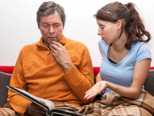 Uomo con espressione preoccupata guarda un album, mentre una donna gli parla con fare interrogativo. Potrebbe trattarsi di demenza senile precoce sintomi.