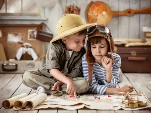 Dos niños planean una aventura en una casa rural para niños, con un mapa, lupa y sombrero de explorador.