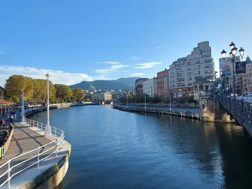 Blick auf den Bilbao Fluss mit Gebäuden und einer Brücke im Hintergrund.