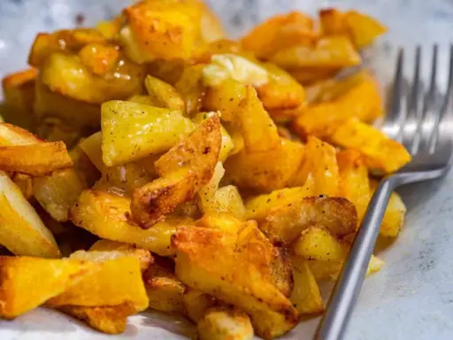 Un plato de patatas asadas doradas y crujientes, sazonadas con hierbas y especias, listas para ser disfrutadas con un tenedor.