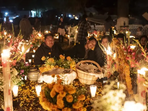 Rodzina przy grobie ozdobionym świecami i kwiatami na Dia de los Muertos.