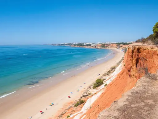 Blick auf den Strand Praia da Falésia mit seinen roten Felsen und der Stadt im Hintergrund.