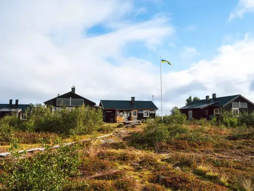 Mörka trähus med solpaneler och en svensk flagga som vajar. Ett charmigt vandrarhem i Dalarna, omgivet av vildmark.