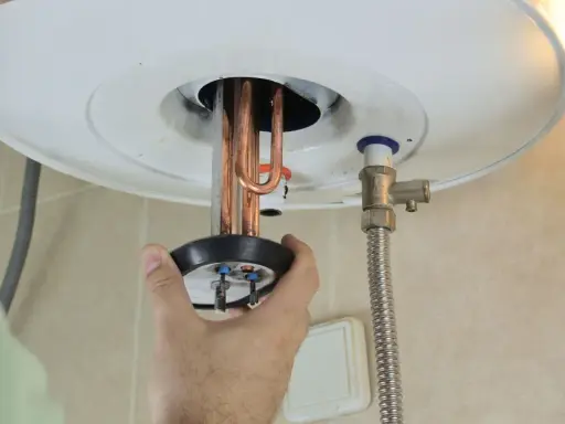 Mano ajustando la resistencia termoeléctrica de un calentador de agua.