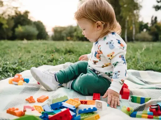 Un niño pequeño juega con bloques de construcción y un coche de juguete en el césped, disfrutando de actividades para niños de 2 a 3 años.