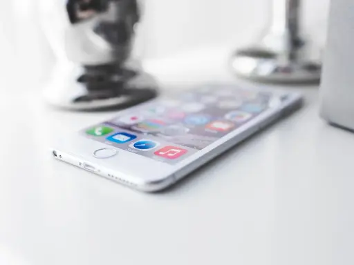Biały iPhone leży na białym blacie, gotowy do pracy. W tle widać błyszczące i matowe elementy dekoracyjne.