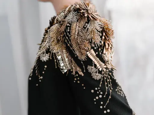 A black garment with an elaborate shoulder embellishment of gold and silver beads, sequins, and crystals, showcasing the definition of embellished fashion.