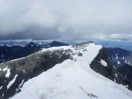 Snöklädda bergstoppar och molniga himlar. En repstump syns i förgrunden, redo för äventyret på Kebnekaise leder.