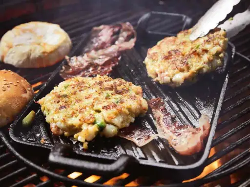 Burger-Patties und Brötchenhälften werden auf einem Grillrost zubereitet. Das Burger grillen verspricht einen köstlichen Genuss.