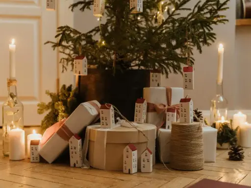 Julkalender tips: En julgran med små hus som dekorationer, presenter och ljus skapar en mysig julstämning.
