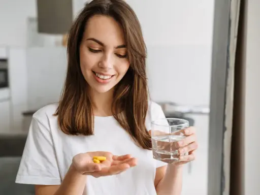 Uśmiechnięta kobieta trzyma w dłoni tabletki preductal mr 35 mg i szklankę wody.