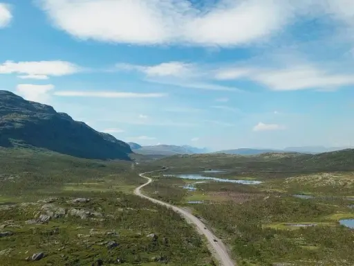 Väg slingrar sig genom ett vidsträckt landskap med berg och sjöar. Perfekt för camping i Norrbotten.
