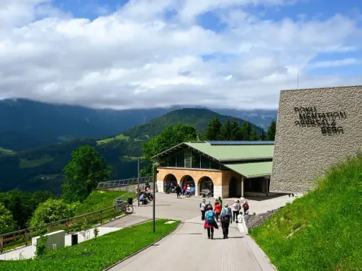 Besucher erkunden das Dokumentationszentrum Obersalzberg, umgeben von grünen Hügeln und Bergen.