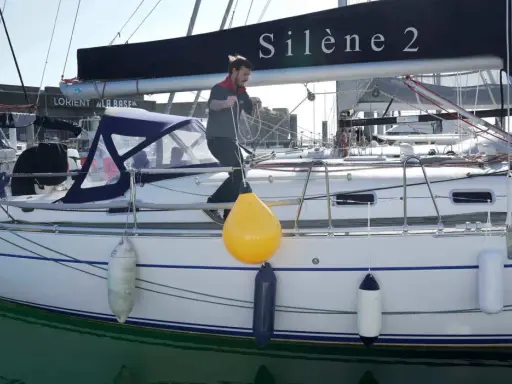 Un homme ajuste un pare-battage jaune sur un voilier. Ces bouées protègent la coque des chocs.