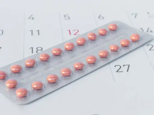 Różne rodzaje tabletek antykoncepcyjnych w blistrze na tle kalendarza.