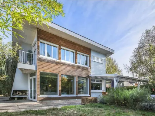Architecture maison année 60 avec bardage bois et grandes baies vitrées, balcon moderne, entourée de verdure.