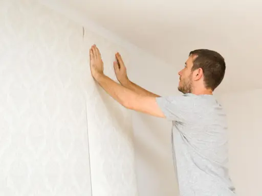 Hombre colocando papel pintado con patrón floral en una pared. Aprende como poner papel pintado tú mismo.