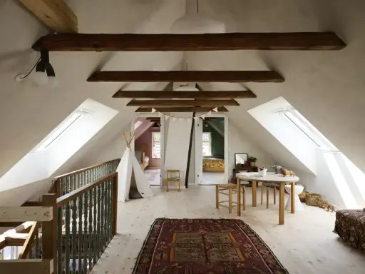 Idee per ristrutturare casa antica: mansarda luminosa con travi a vista, tappeto persiano, teepee e tavolino per bambini.