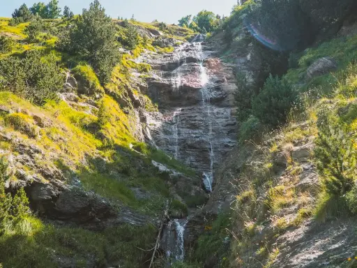 Cascada cayendo por una ladera rocosa, rodeada de vegetación verde y amarilla. Un hermoso paisaje que invita a recorrer la ruta de las tres cascadas.