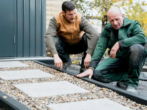 Zwei Männer arbeiten an einer neuen kies terrasse mit quadratischen Trittsteinen.