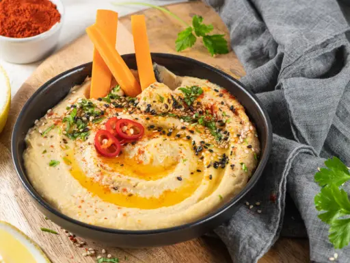 Hummus cremoso con bastones de zanahoria, pimientos rojos y semillas. Un snack saludable ideal para el embarazo.