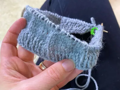 En hand håller ett stickat provstycke i ljusgrått garn. Tekniken german short rows används för att forma det.