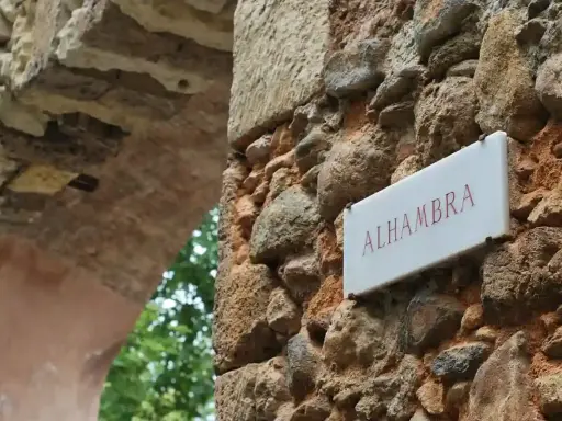 Schild "Alhambra" an einer alten Steinmauer, die zu einem Parkplatz führt.