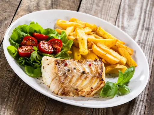 Idealne jakie przyprawy do ryby? Pieprz i sól na grillowanym filecie, obok frytki i sałatka z pomidorkami.