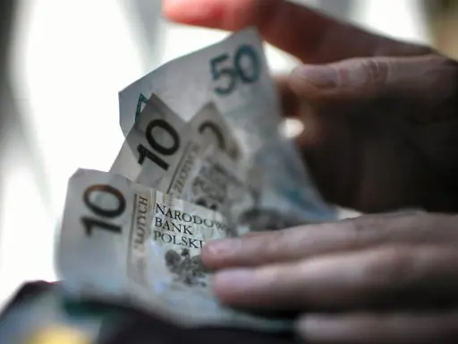 Dłoń trzyma polskie banknoty 10 i 50 zł. Zastanawiasz się, ile pieniędzy na bierzmowanie to odpowiednia kwota?
