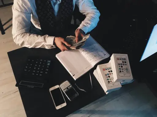 Mężczyzna liczy pieniądze, obok leżą telefony i kalkulator. To może być pomocne, jak udowodnić pochodzenie pieniędzy.
